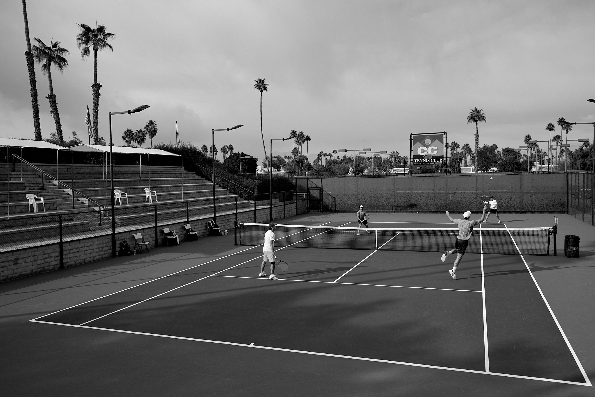 Doubles match with the CC Tennis Club sign visible through the fence